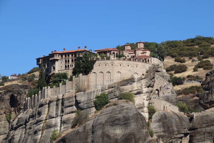 Monastery perched atop towering sandstone cliffs at Meteora under clear blue sky.