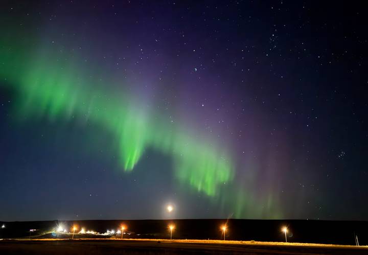 Northern Lights dancing in green and purple hues over a dark horizon and star-filled sky.