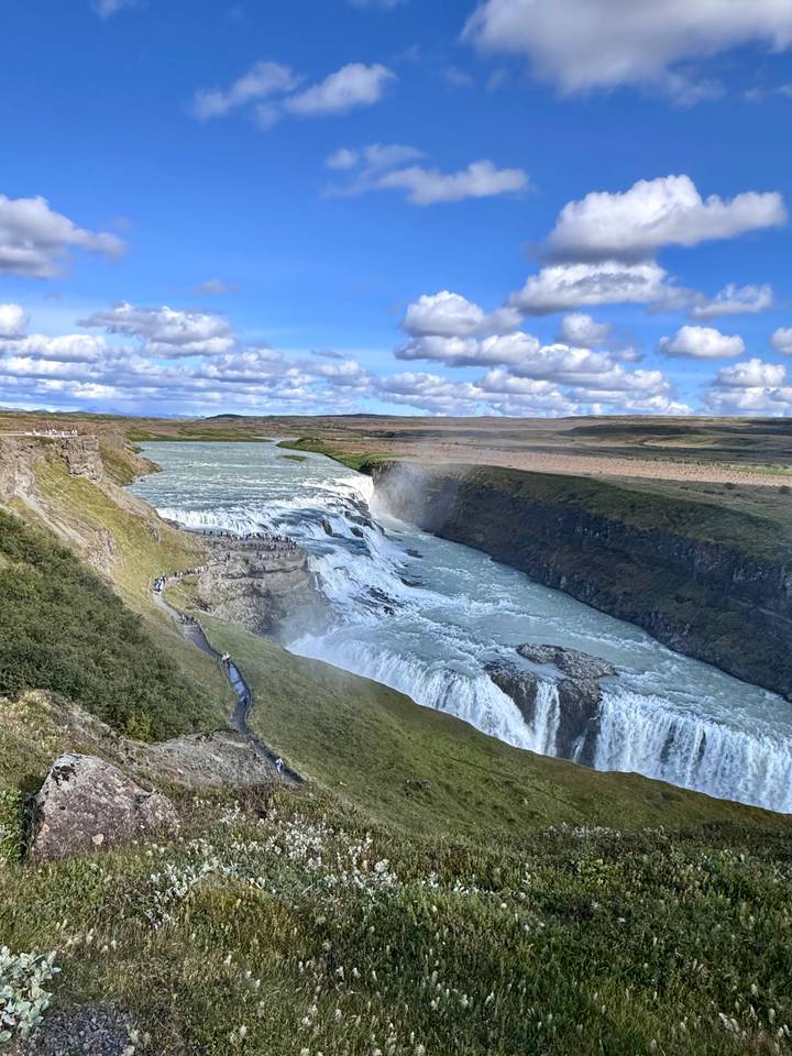 Sweeping view of Gullfoss waterfall plunging into a rugged canyon amid green Icelandic plains.