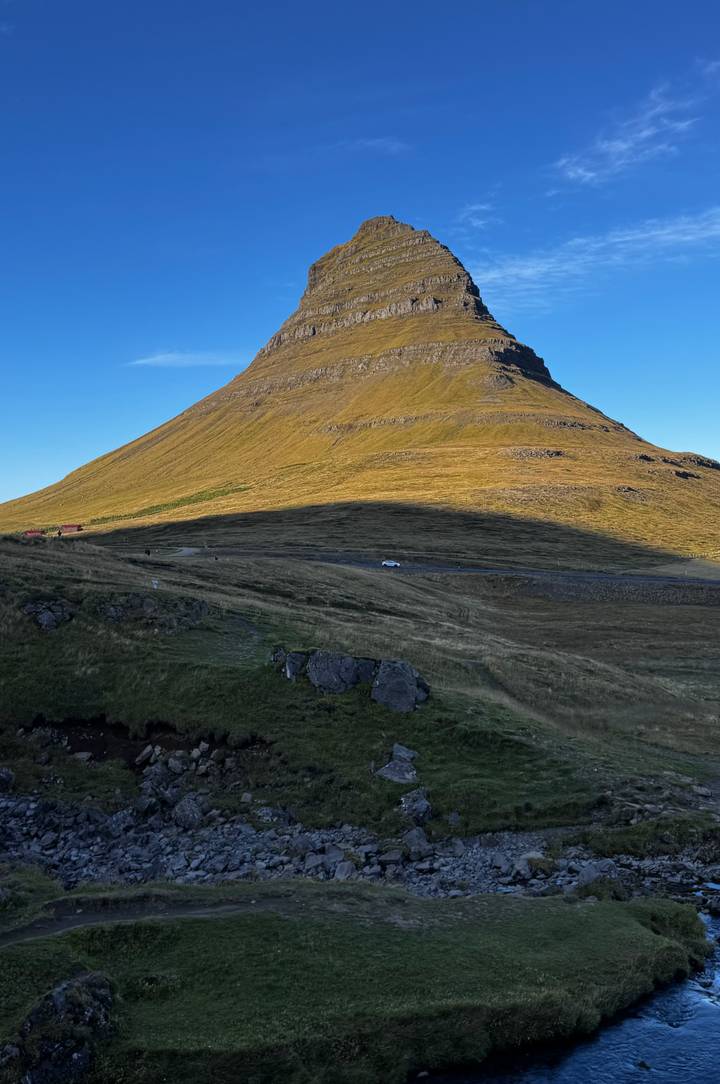 Distinctive cone-shaped Kirkjufell mountain lit by late-day sunlight with rugged grassy foreground.