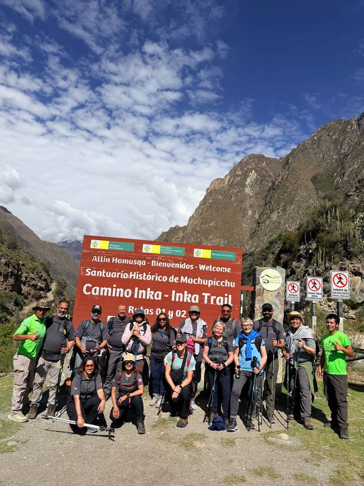 Hiking group posing at the Camino Inka – Inka Trail welcome sign beside rugged valley walls.