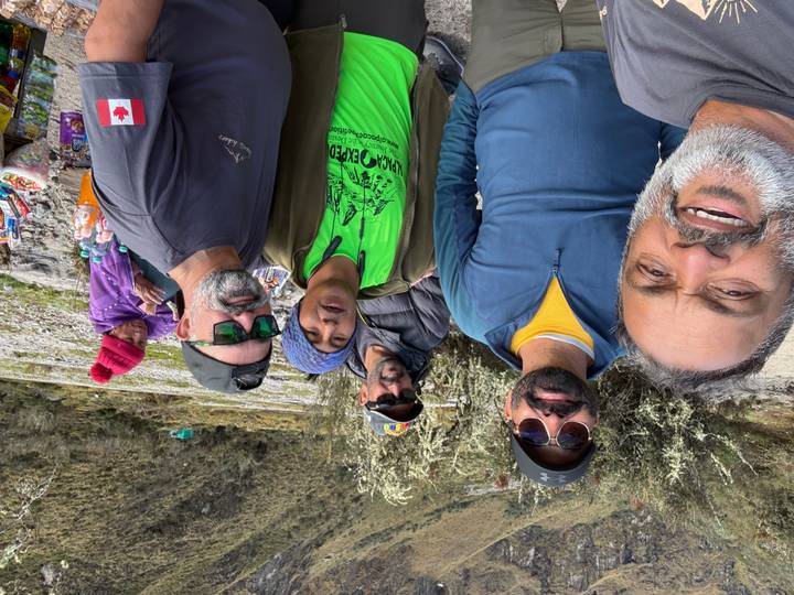 Casual selfie of trekkers at a rest stop with snacks table and mountain vegetation around.
