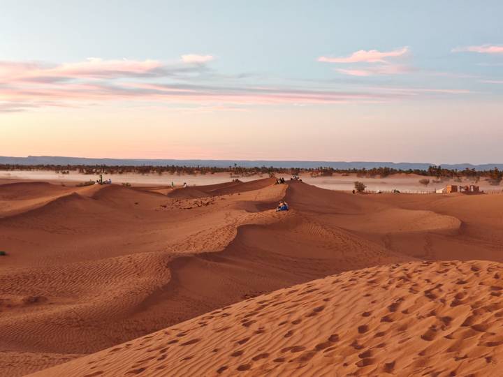 Sunrise glow over sand dunes of the Sahara near Merzouga with low mist hovering and distant riders.