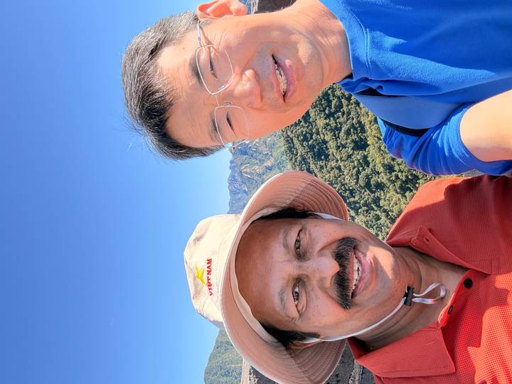 Duplicate selfie of two travelers with green mountains under a bright sky