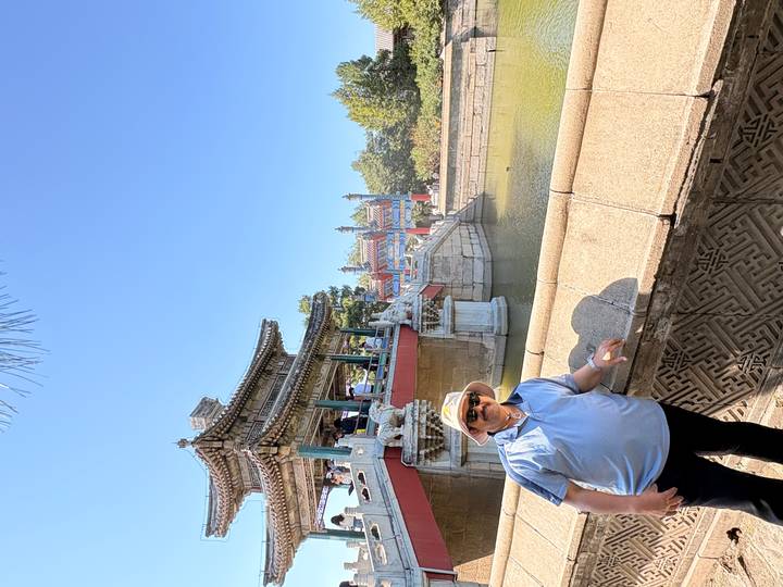 Traveler posing beside a traditional Chinese pavilion over a moat on a bright day