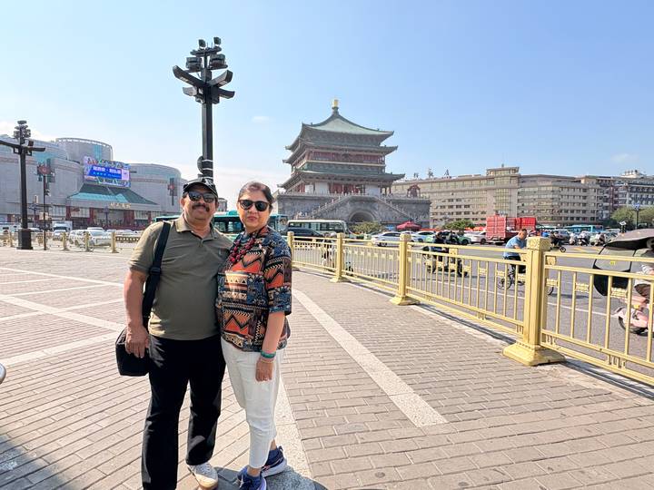 Couple standing in a plaza with Xi'an Bell Tower and traffic behind them