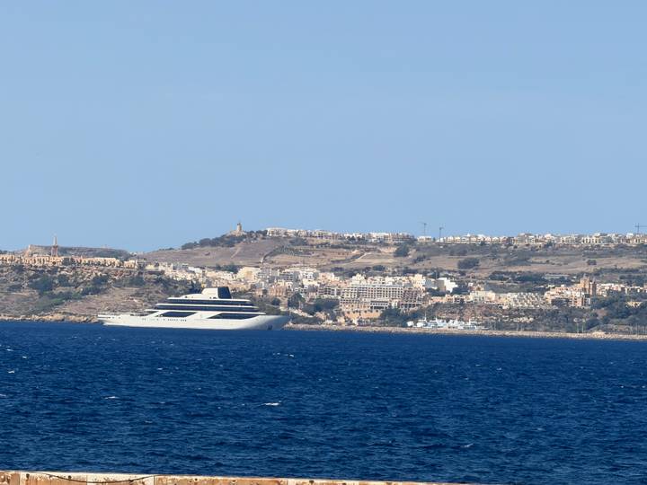 Distant coastal Maltese town with large luxury yacht on deep blue Mediterranean Sea