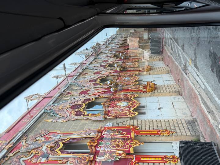 Colorful ornate festival facade panels stored along a street, photographed through a bus window