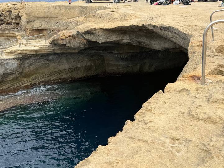 Rocky coastal cave opening with dark blue water at the Blue Grotto area