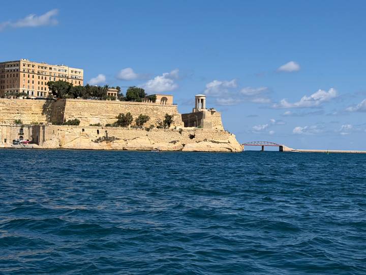Stone fortifications and small arch bridge along the Maltese coastline seen from the sea