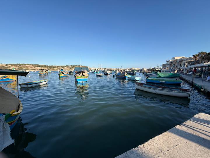 Colorful traditional fishing boats moored in a calm Maltese harbour under clear sky
