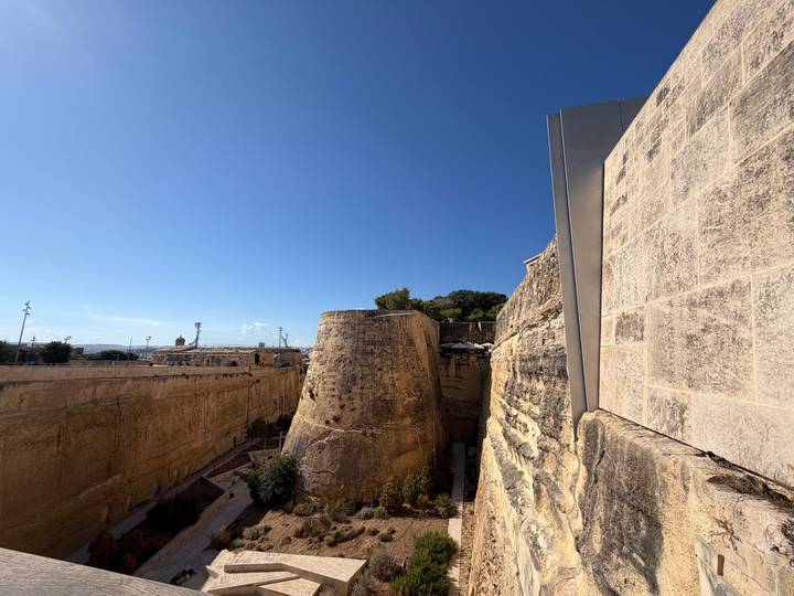 Massive limestone defensive walls and dry moat under clear blue sky