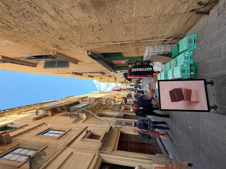 Narrow Maltese street lined with honey-colored buildings, shops and tourists walking