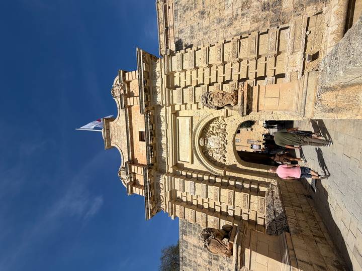 Stone gateway entrance to Mdina with tourists walking beneath a clear blue sky