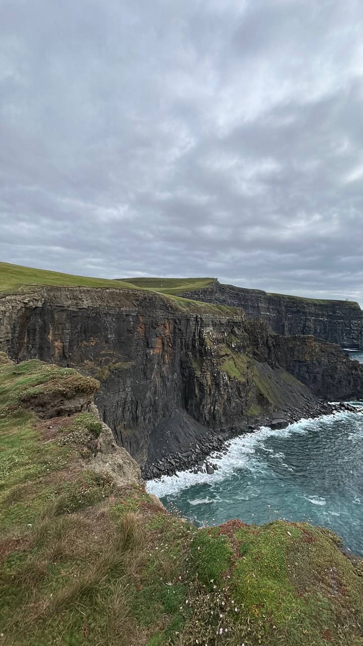 Dramatic sheer cliffs plunging into the Atlantic Ocean at the Cliffs of Moher under overcast skies.