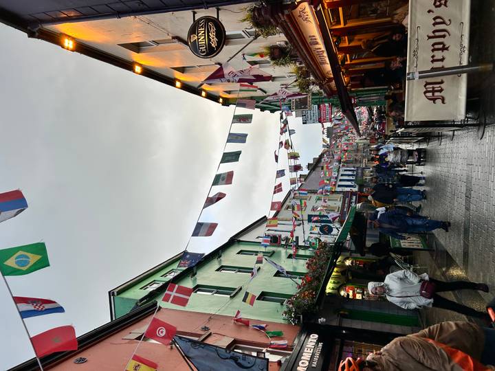 Colorful pedestrian street lined with Irish pubs and shops, festooned with international flags on a damp evening