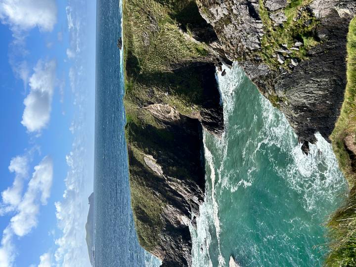 Dramatic sea cliffs and turquoise Atlantic waters with waves crashing below a grassy headland