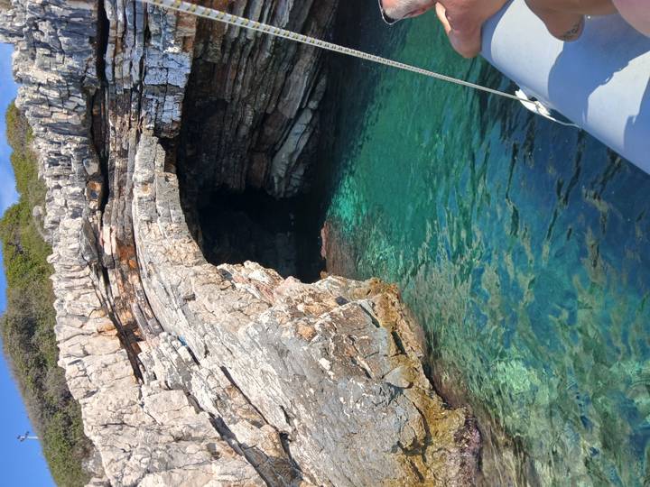 Clear turquoise water at the entrance of a rocky coastal cave seen from a small boat.