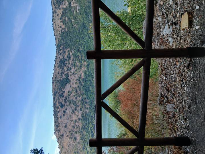 View across wooden railing toward blue-green mountain lake and dry hillside vegetation.