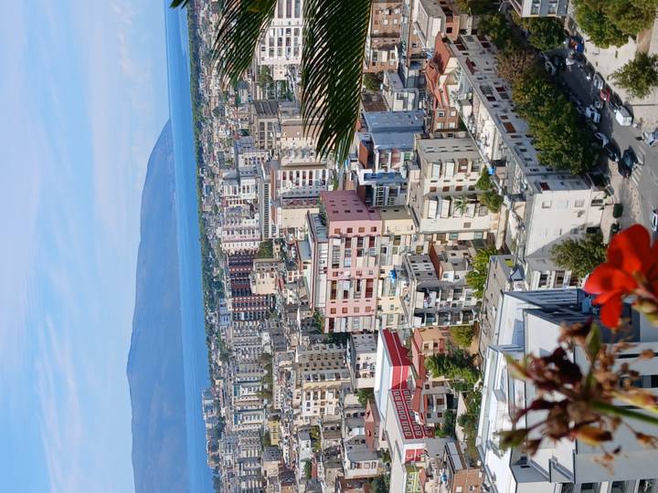 High viewpoint of a coastal Albanian city with apartment blocks, bay and mountains in the distance.