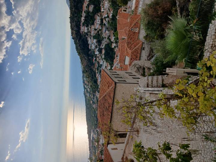 Terracotta-roofed hillside village descending toward a shimmering sea at golden hour.