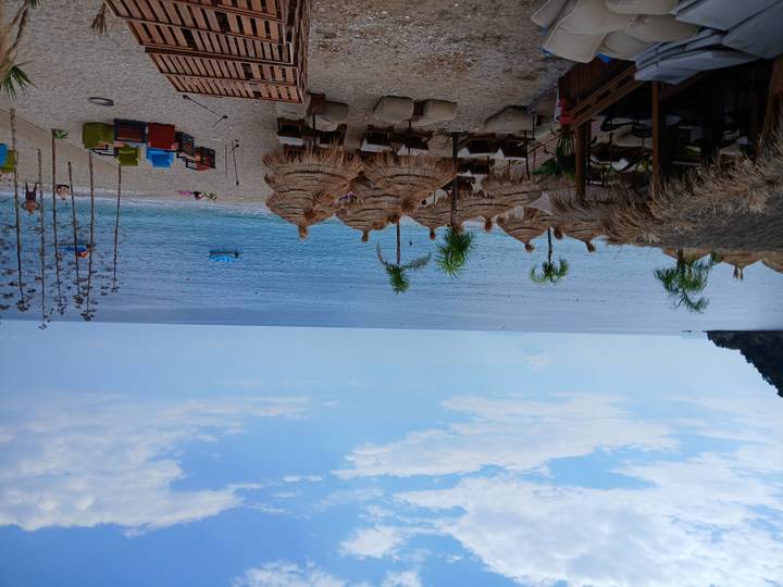Sandy beach with thatched umbrellas, loungers and a beach bar facing calm blue waters.