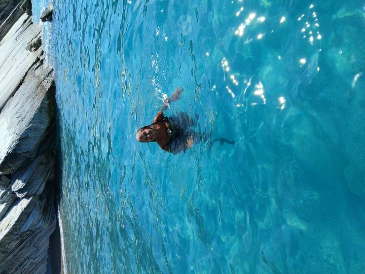Woman happily swimming in crystal-clear blue water beside a rocky shoreline.