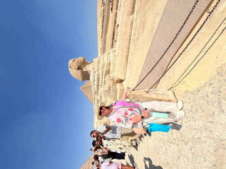 Tourist poses beside the Great Sphinx with a tour group gathered nearby under bright desert sun.