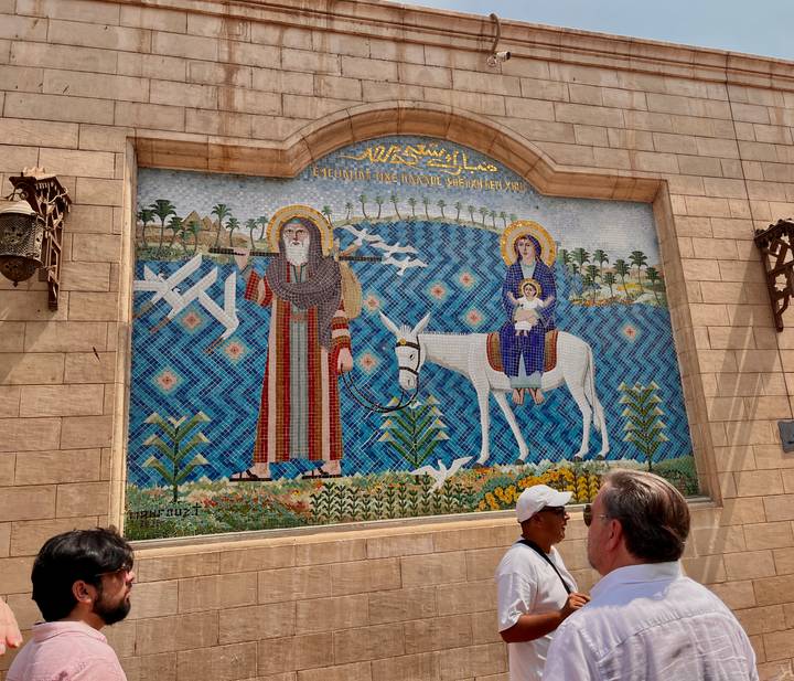 Colourful mosaic depicting the Holy Family on a donkey adorns a stone church wall as tourists observe.