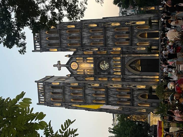 Evening crowd gathers before Hanoi’s neo-gothic St. Joseph Cathedral, warmly lit against dusk sky.