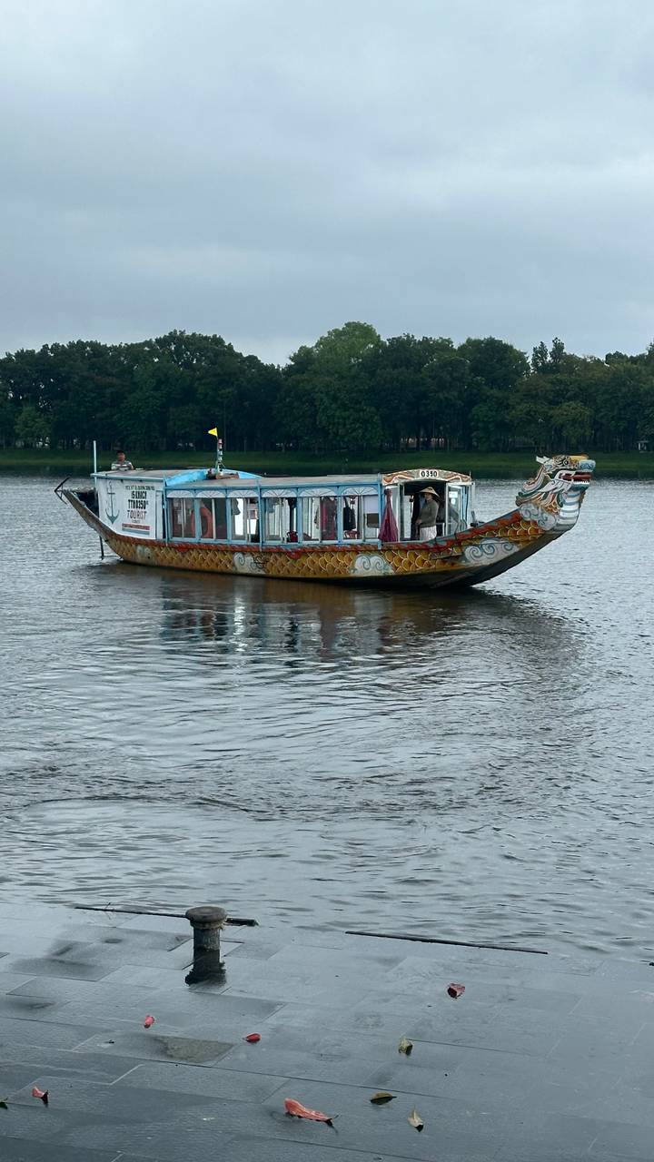 Decorative dragon boat ferry cruising along a calm river with tree-lined banks