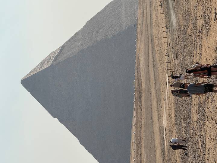 Tourists walking toward the massive pyramid rising from the desert plateau on a hazy day