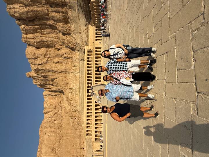 A group of travelers pose in front of Hatshepsut’s mortuary temple with towering cliffs behind.