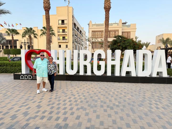 An older couple smiles beside a large I-Love-Hurghada sign in a modern plaza at dusk.