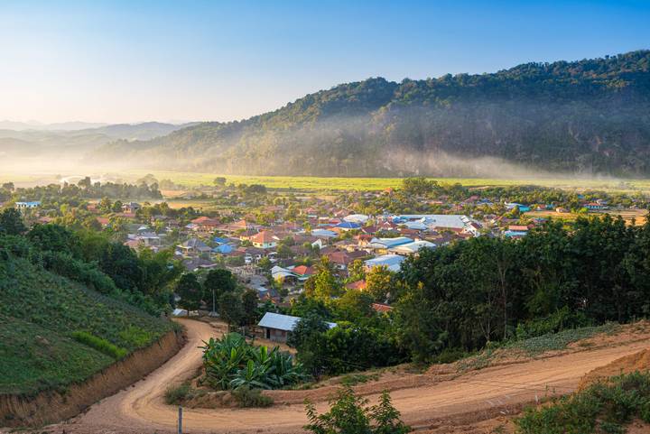 Early-morning mist hangs over a valley town surrounded by lush green mountains in northern Laos.