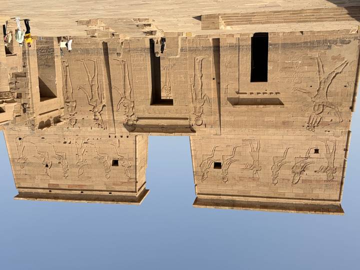 Facade of Philae Temple with large sunken reliefs while visitors explore the entrance.