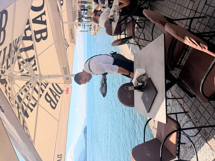 Waiter setting a table under a parasol beside a tranquil lakefront café