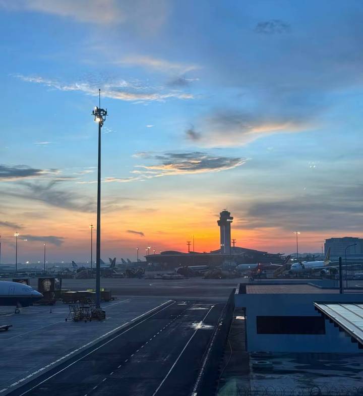Airport apron at dawn with control tower silhouette and planes parked under a colourful sunrise sky