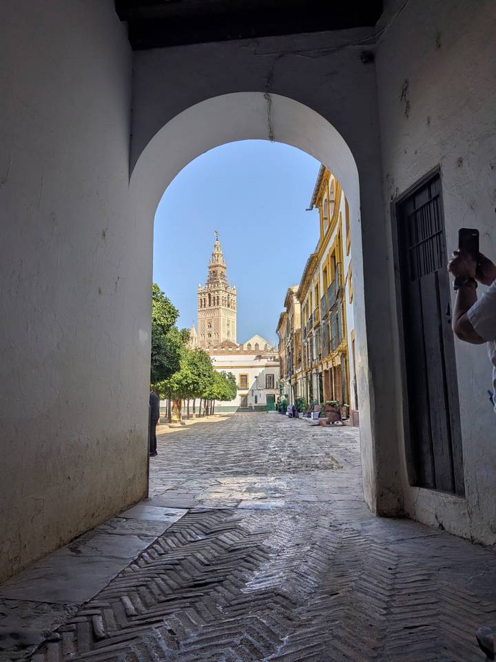 View through a white archway to Seville’s Giralda bell tower rising above a quiet cobbled street lined with historic buildings.