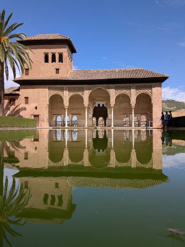Elegant Moorish arches of the Alhambra reflected perfectly in a tranquil green pool on a bright day.