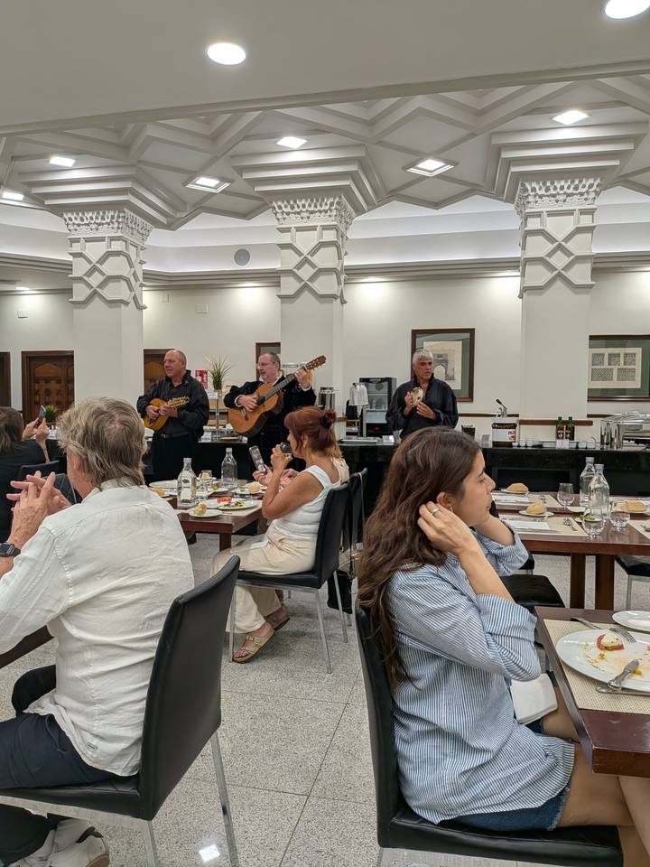 Guests dine while three musicians in traditional black outfits play guitars and mandolins inside a bright restaurant.