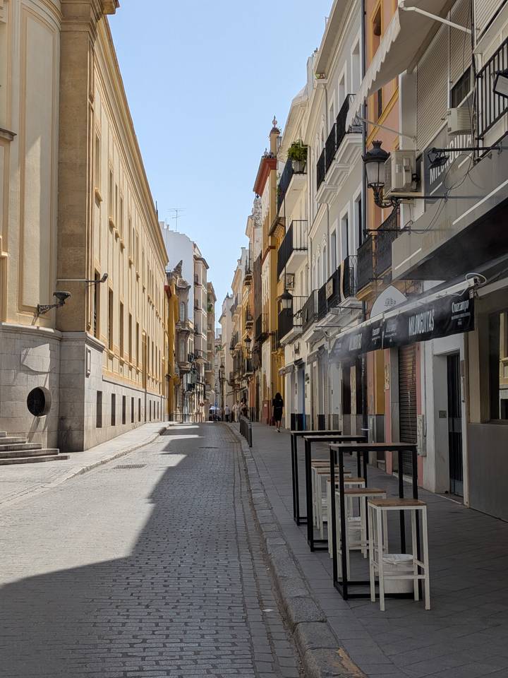 A mist-cooled pedestrian lane lined with tall classic buildings painted in warm tones under bright sun.