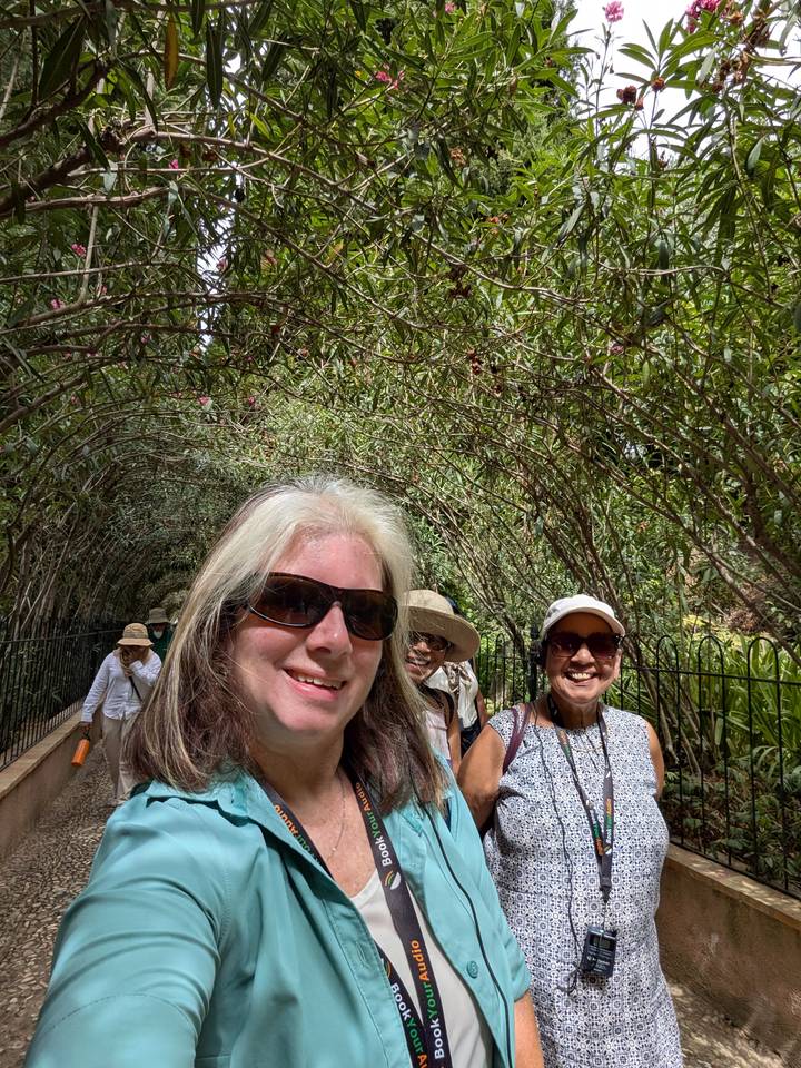 Smiling travellers take a selfie while walking under a leafy tunnel of intertwined branches.