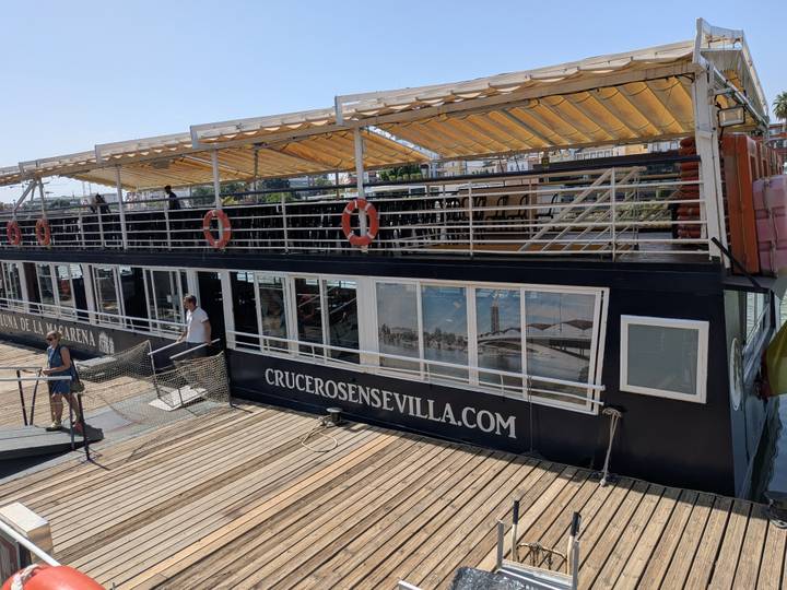 A docked black river cruise boat advertising crucerosensevilla.com with crew preparing the gangway.