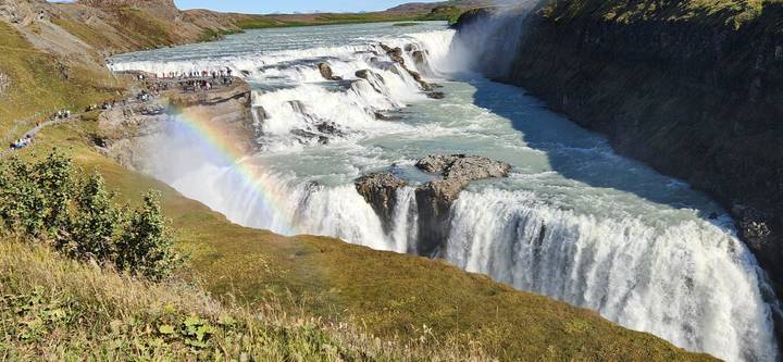 Powerful tiers of Gullfoss waterfall crash into a canyon with a vivid rainbow arcing through the spray.