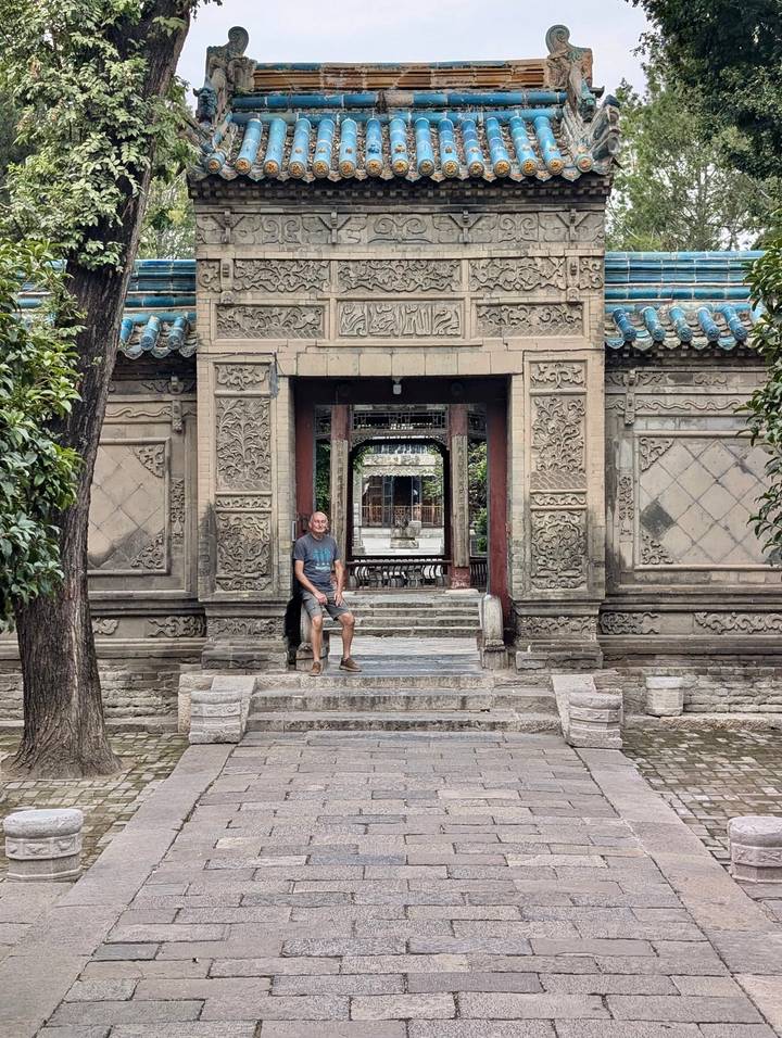 A traveller sits on stone steps framed by ornate carved gateways in a historic Chinese courtyard.