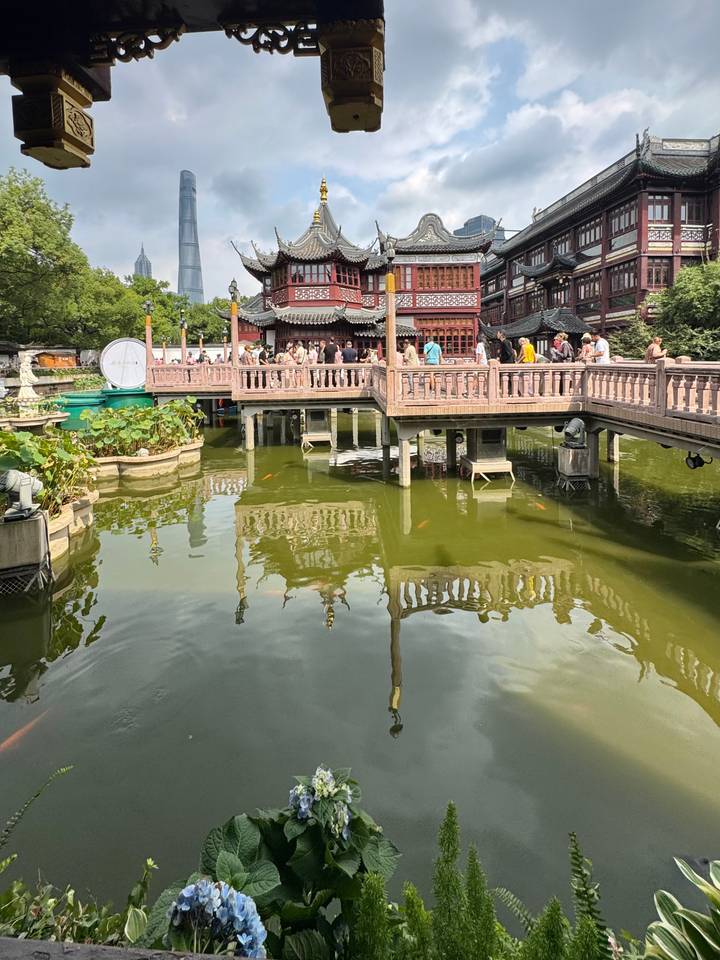 Crowds stroll across ornate wooden bridges over a koi-filled pond in the classical Yu Garden complex.