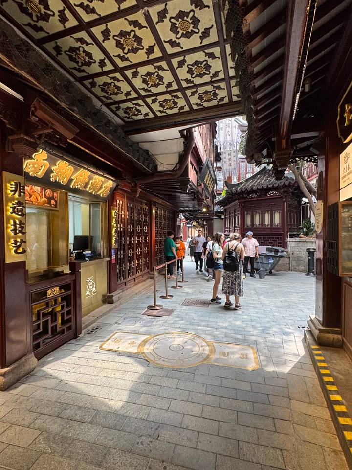 Narrow pedestrian lane in a traditional Chinese bazaar with wooden facades, lantern signs and visitors lining up.