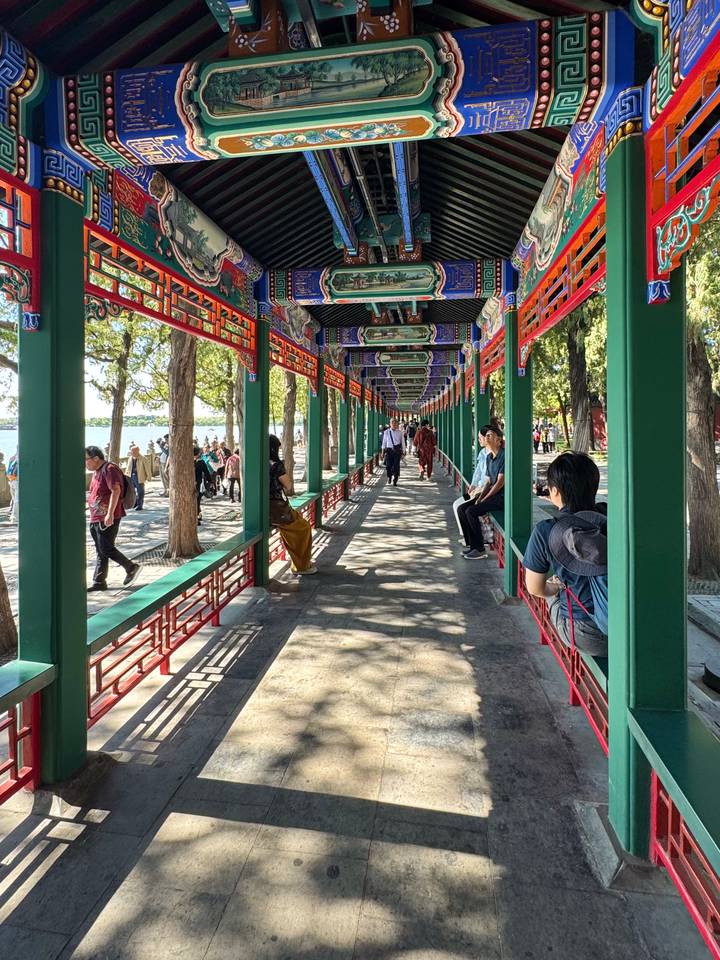 Long, colorfully painted covered walkway lined with green pillars and red lattices at the Summer Palace lakefront.