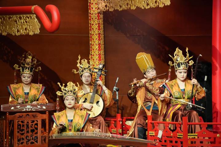 Traditional Chinese orchestra in ornate golden costumes performing on stage with classical instruments.